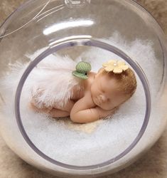 a baby doll is in a glass bowl with white fur and green leaves on its head