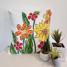 a pillow with flowers painted on it next to a potted succulent plant