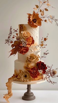 a three tiered cake with flowers and leaves on it's side, sitting on top of a table