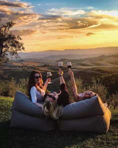 two women are sitting on a bean bag and toasting with wine glasses in their hands