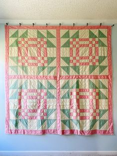 a pink and green quilt hanging on the wall