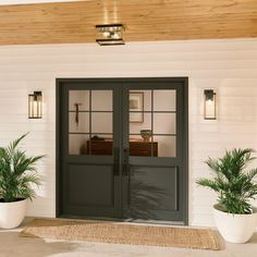 two potted plants sitting on top of a door mat in front of a white house