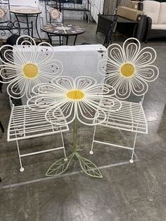 a white metal chair with yellow flowers on it's back and sides, sitting in a warehouse