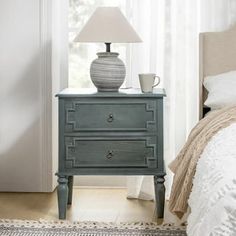 a nightstand with a lamp on top of it next to a bed in a bedroom