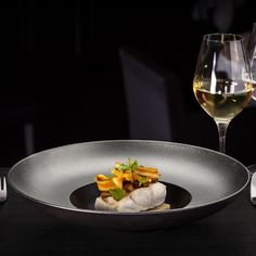 a glass of wine and some food in a bowl on a table with utensils