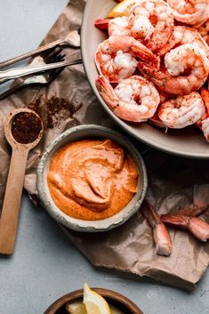 a bowl filled with shrimp next to some dipping sauce and lemon wedges on the side