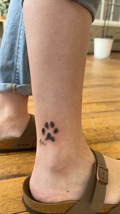 a person with a dog paw tattoo on their foot, standing in front of a wooden floor