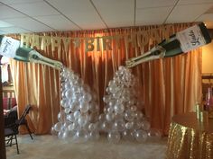 two champagne bottles on top of balloons in front of a happy birthday banner and curtain