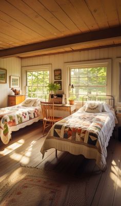 two beds in a room with wooden floors and windows on each side, one has a quilt on the bed