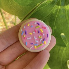 a hand holding a pink frosted donut with sprinkles on it