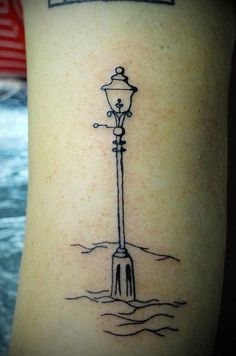 a black and white photo of a lamp post on the side of a woman's arm