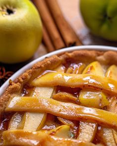 an apple pie on a plate with cinnamon sticks and apples in the background, all around it