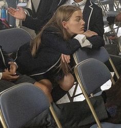 a woman sitting in a row of chairs with her head resting on her hand and other people standing behind her