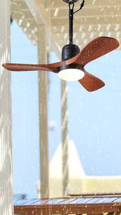 a ceiling fan that is hanging from the ceiling in front of a window with rain falling on it