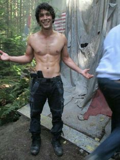 a shirtless man standing in the woods with his hands out and one hand out