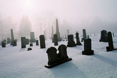 black and white photo of an old cemetery in the snow with tombstones on it