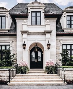 a large white house with two black doors and some pink flowers on the front steps