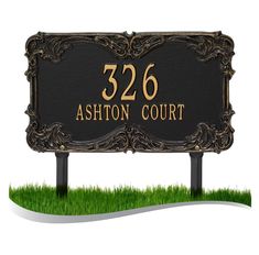 a black and gold address sign sitting on top of green grass