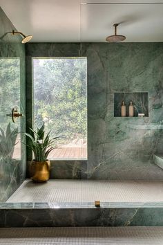 a bathroom with green marble walls and flooring next to a large window that looks out onto the outdoors