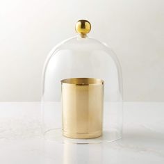 a gold cup under a glass dome on a white counter top, with the lid partially closed