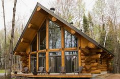 a small log cabin in the woods with chairs on the front porch and large windows