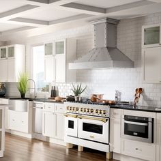 a kitchen with white cabinets and black counter tops, an oven and stove hood in the center