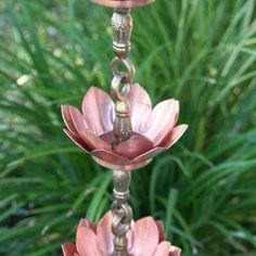 three pink flowers are hanging from a metal pole in front of some green grass and plants