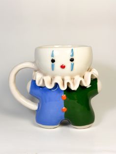 two ceramic mugs with faces on them sitting side by side, one is green and the other is blue