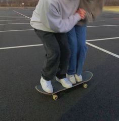 two people riding on top of a skateboard in an empty parking lot at dusk