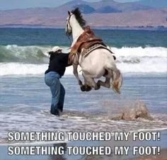 a man is riding a horse on the beach with his feet in the water while another person watches