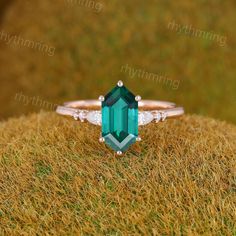 an emerald colored stone ring with diamond accents on top of the band, sitting on grass