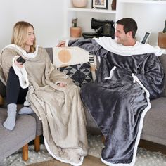 a man and woman sitting on a couch covered in blankets