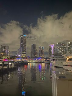 the city skyline is lit up at night with lights reflecting in the water and clouds