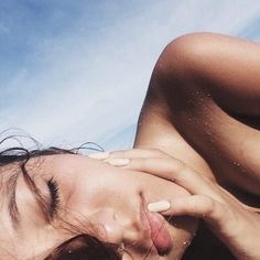 a woman laying on top of a sandy beach next to the ocean with her eyes closed