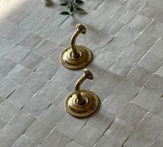 two brass hooks sitting on top of a white tile floor next to a flower