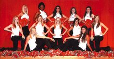 the cheerleaders are posing for a group photo in front of a red background