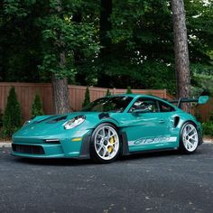 a green sports car parked in front of a wooden fence and tree lined driveway area