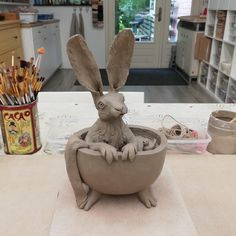 a clay sculpture of a rabbit in a bowl with colored pencils on the table