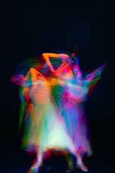 three women dancing in the dark with colored lights on their body and arms, all holding hands together