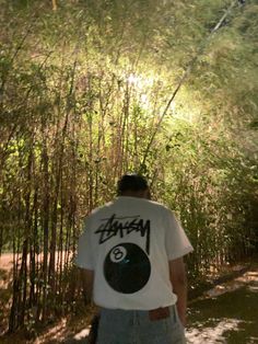 a man walking down a dirt road next to tall grass and bamboo trees in the background