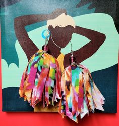 a pair of colorful tasselled earrings hanging from a hook on a red background