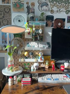 a desk with a computer, keyboard and various other items on it in front of a wall full of pictures