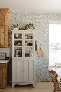 a kitchen area with a china cabinet, table and wooden chairs next to a window