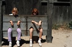 two children sitting on a wooden bench with their hands in the back and legs crossed