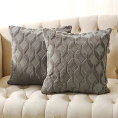 two gray pillows sitting on top of a white couch