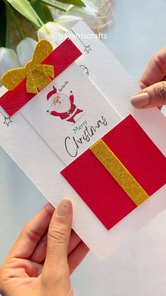 two hands holding an open christmas card with a bow on the front, and a red envelope with gold ribbon