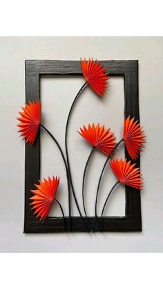 an art piece with orange paper flowers in a black frame on a white wall behind it