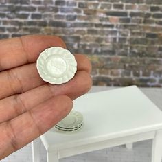 a hand holding a small white object in front of a brick wall and table with plates on it