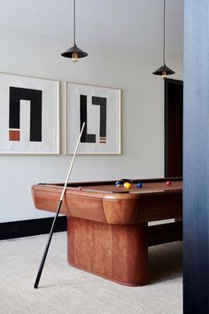 a pool table in a room with two pictures on the wall and a pool cue