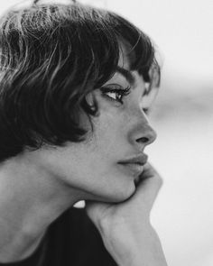 a black and white photo of a woman with her hand on her chin looking off to the side